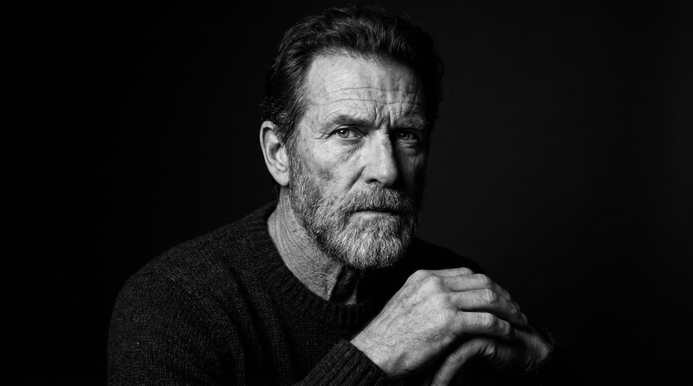 Retrato en blanco y negro de un hombre mayor con barba gris, iluminado por una luz lateral dura sobre un fondo oscuro.
